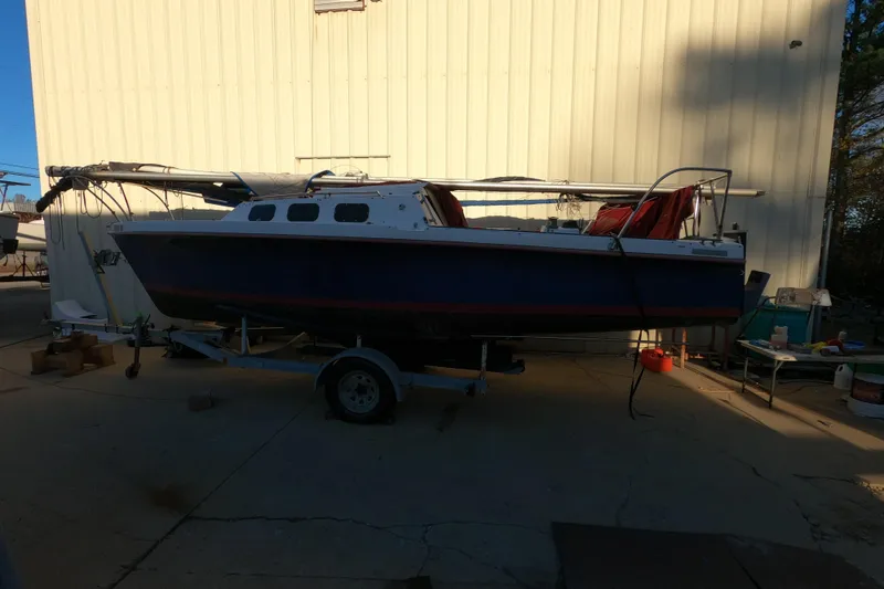 Slide: The Image of 1986 Rhodes 22 sailboat on trailer, parked beside a building in a sunny outdoor setting. - 19
