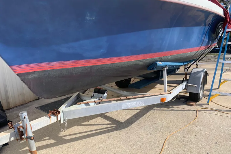 Slide: The Image of 1986 Rhodes 22 sailboat on trailer, blue hull with red stripe, parked outdoors. - 3