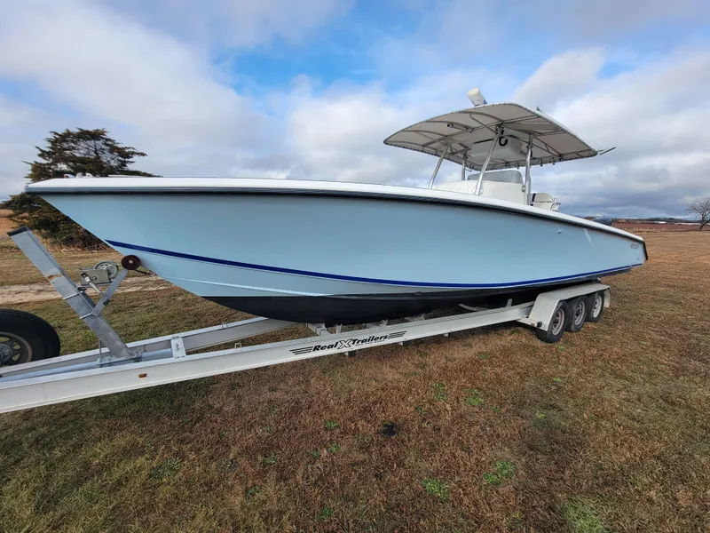 The Image of 1996 Venture 34 Center Console boat on trailer, parked on grassy field under cloudy sky. - 0