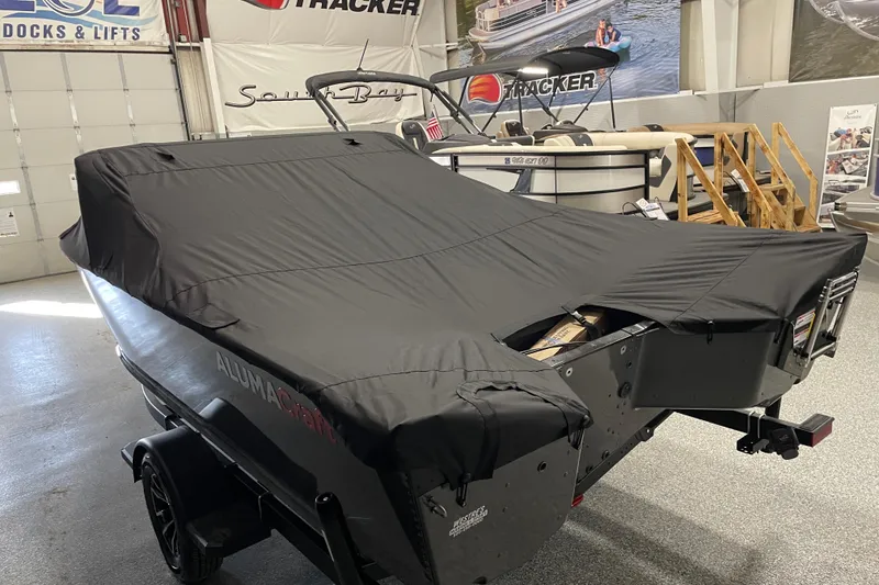 Slide: The Image of 2026 Alumacraft Competitor 185X Sport boat covered in black tarp, displayed indoors. - 17