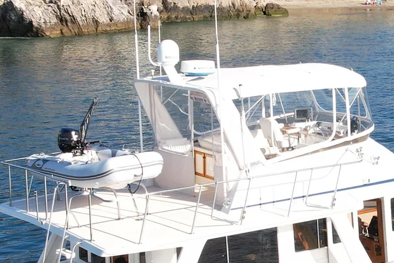 Slide: The Image of 1997 Offshore Yachts 48 Sedan with dinghy on deck, anchored near rocky shoreline. - 11