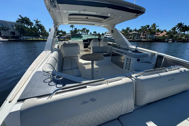 Slide: The Image of 2022 Sea Ray SLX 400 Outboard luxury boat interior with seating and table, docked by palm trees. - 14