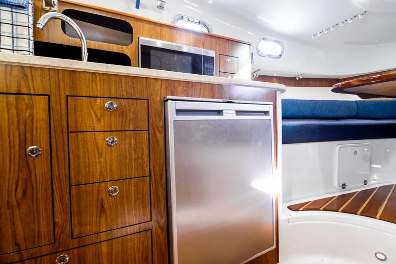 Slide: The Image of 2013 Pursuit OS 345 Offshore boat interior with wood cabinetry, fridge, and seating area. - 9
