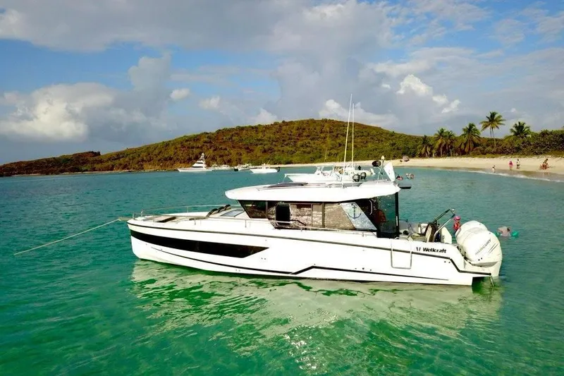 Slide: The Image of 2023 Wellcraft 355 boat anchored near tropical beach with clear turquoise water. - 2