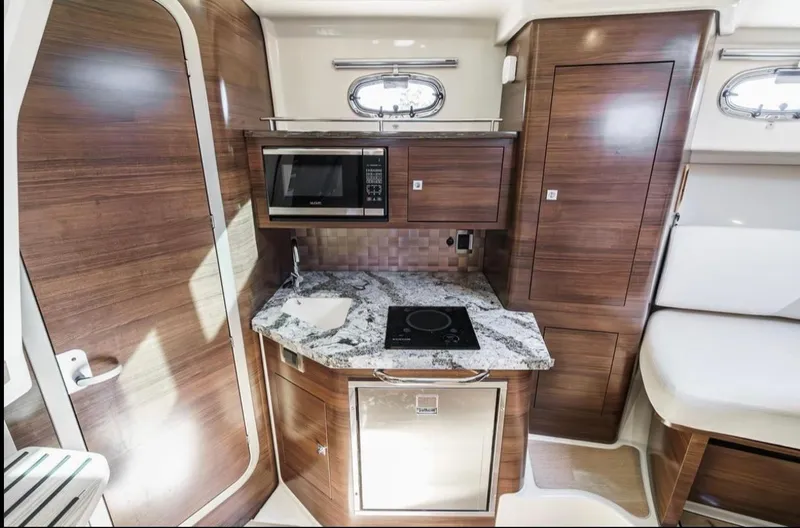 Slide: The Image of 2019 Boston Whaler 345 Conquest interior kitchen with microwave, stove, and wood cabinetry. - 16