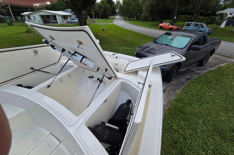 Slide: The Image of 2023 Mako Pro Skiff 19 CC with open storage compartments, parked near a gray truck. - 19