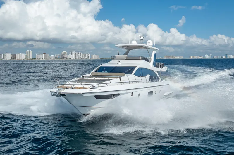 Slide: The Image of 2019 Azimut 66 yacht cruising on open water with city skyline backdrop. - 16