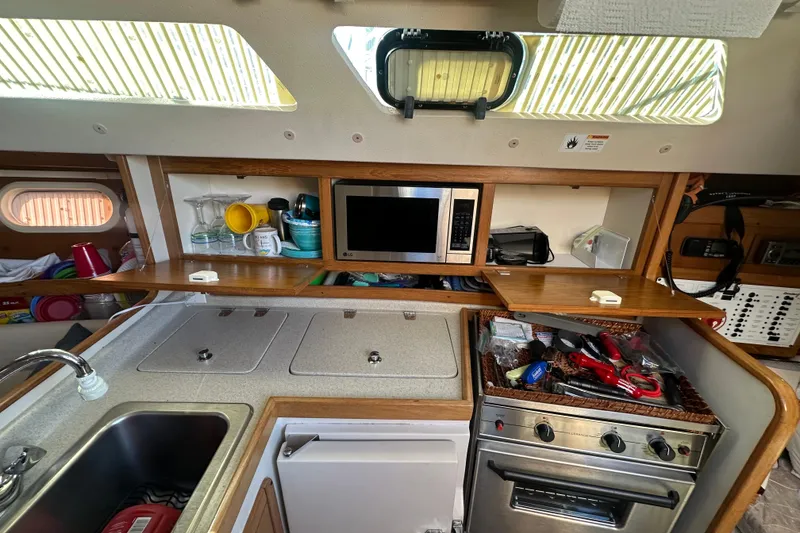 Slide: The Image of 2005 Catalina 310 yacht kitchen with sink, stove, microwave, and storage shelves. - 17