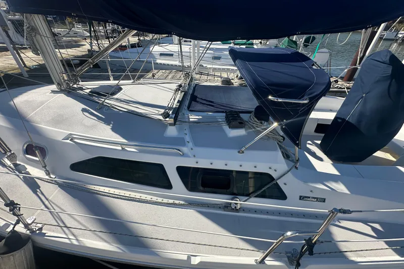 Slide: The Image of 2005 Catalina 310 sailboat docked, featuring sleek design and covered cockpit area. - 2