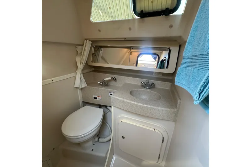 Slide: The Image of 2005 Catalina 310 boat bathroom with sink, toilet, mirror, and blue towel. - 31
