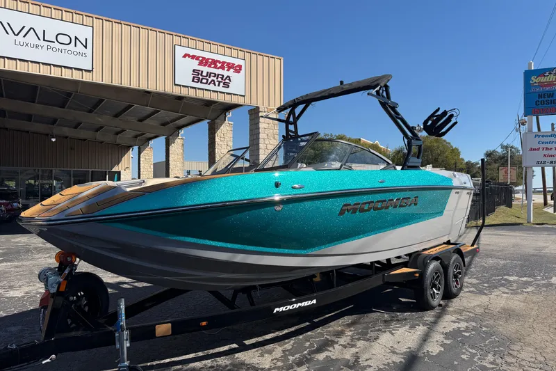 The Image of 2026 Moomba Mojo boat in teal, parked at a dealership with trailers. - 1