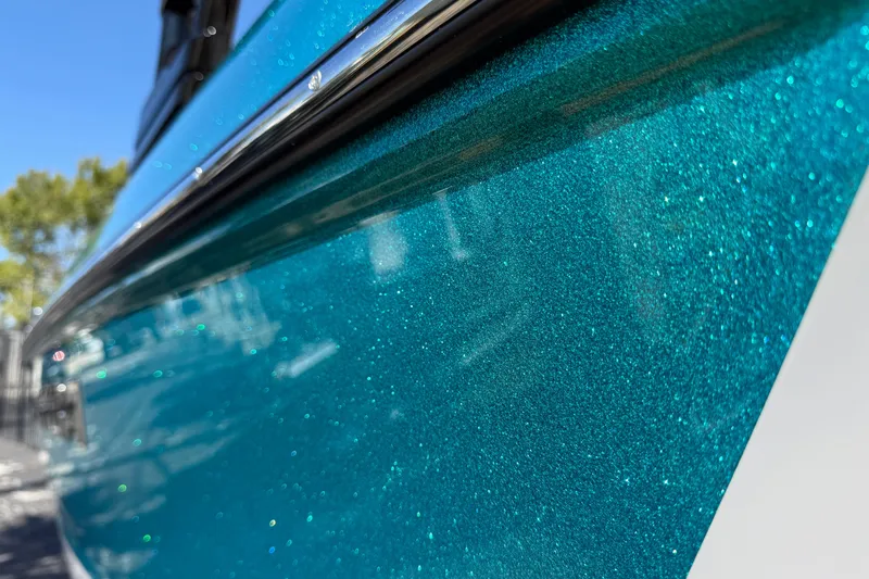 Slide: The Image of 2026 Moomba Mojo boat with sparkling teal finish under clear blue sky. - 10