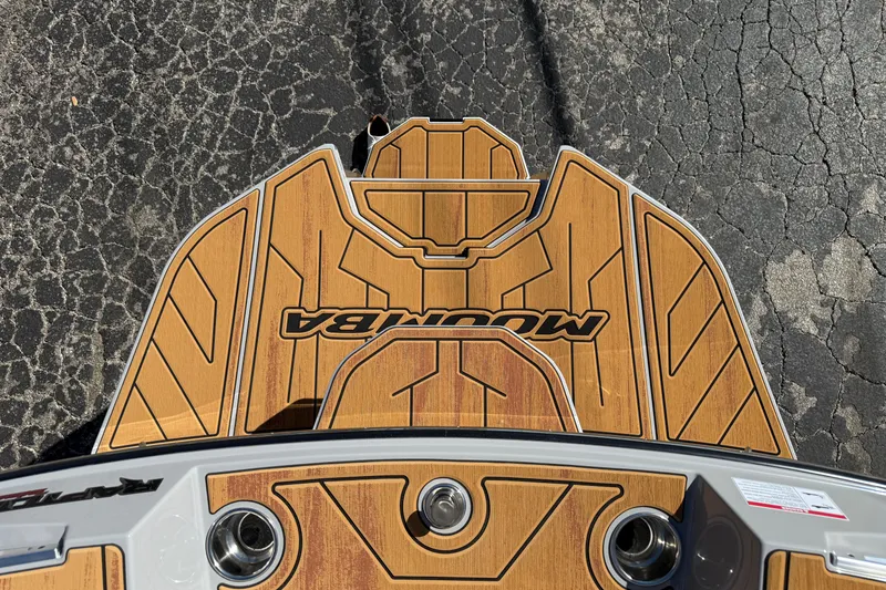 Slide: The Image of 2026 Moomba Mojo boat deck with wood finish and logo, on cracked pavement. - 14
