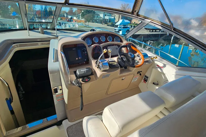 Slide: The Image of 2004 Sea Ray 320 Sundancer cockpit with white seating and control panel, overlooking marina. - 9
