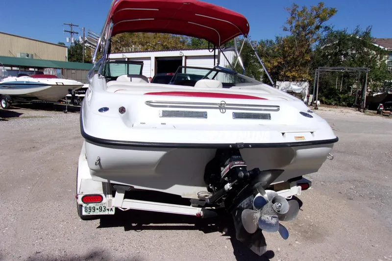 Slide: The Image of 2002 Crownline 202 BR boat with red canopy, parked on a trailer in a lot. - 3