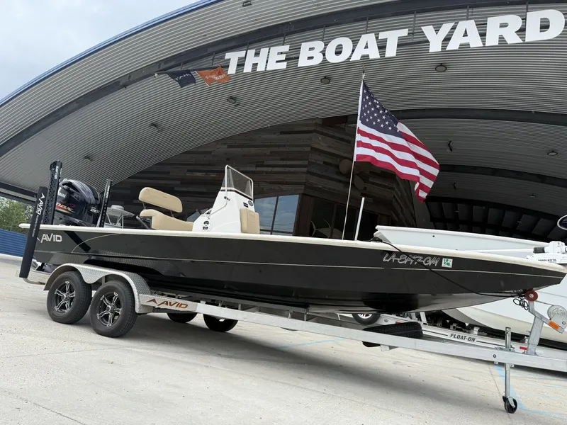 Slide: The Image of 2020 Avid 23 FS boat on trailer, parked outside a modern building under a cloudy sky. - 12