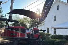 The Image of 2025 Avalon LSZ Quad Lounger Shift boat displayed outdoors with canopy and flags. - 0