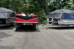 Slide: The Image of 2025 Avalon LSZ Quad Lounger Shift pontoon boat parked with cover, surrounded by trees. - 8