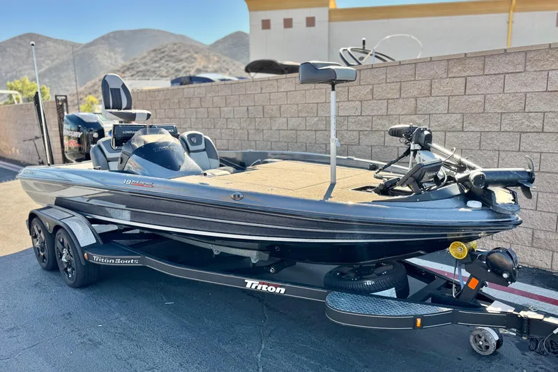 Slide: The Image of 2018 Triton 19 TrX Patriot bass boat on trailer, parked outdoors. - 1