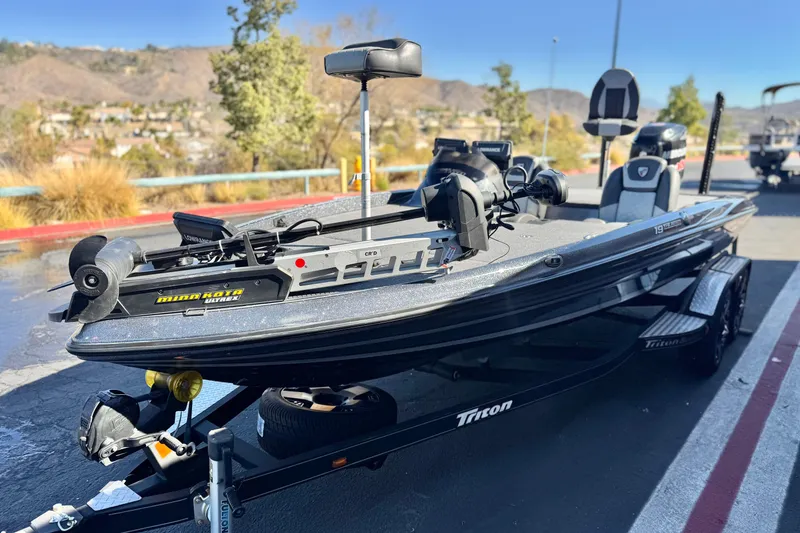 Slide: The Image of 2018 Triton 19 TrX Patriot bass boat with Minn Kota trolling motor, parked outdoors. - 3