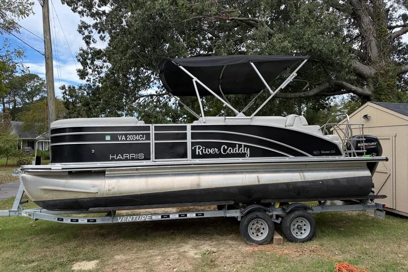 The Image of 2021 Harris Cruiser 210 pontoon boat on trailer, labeled "River Caddy," parked outdoors. - 0