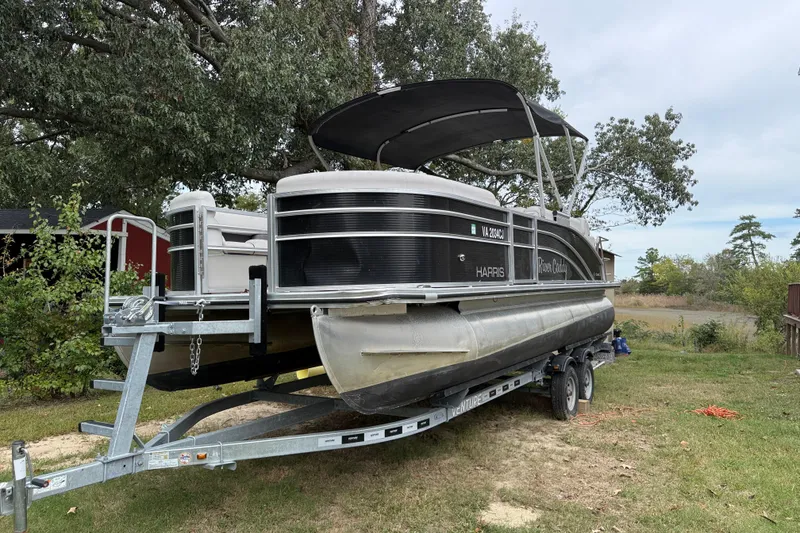 Slide: The Image of 2021 Harris Cruiser 210 pontoon boat on trailer, parked outdoors under trees. - 2