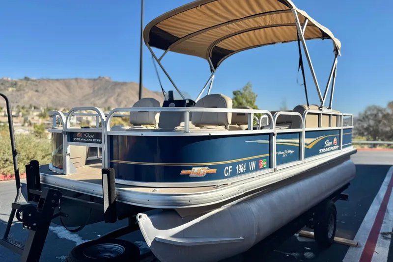 Slide: The Image of 2023 Sun Tracker Bass Buggy 18 DLX pontoon boat on trailer, scenic background. - 3