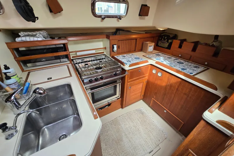 Slide: The Image of Island Packet 420 yacht kitchen interior, 2001 model, featuring stove, sink, and wooden cabinetry. - 32
