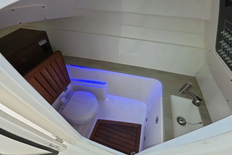 Slide: The Image of 2018 Boston Whaler 320 Vantage boat interior with toilet and sink, featuring blue ambient lighting. - 15