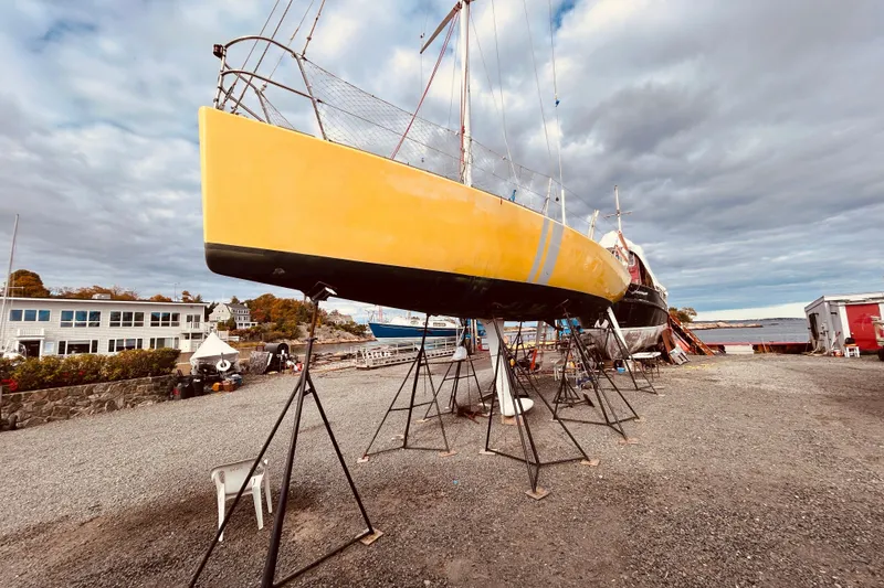The Image of Yellow 2003 Beneteau Figaro 2 sailboat on stands, cloudy sky, waterfront setting. - 0