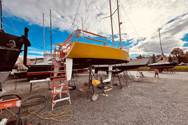 Slide: The Image of 2003 Beneteau Figaro 2 sailboat in dry dock, vibrant yellow hull, clear sky background. - 4