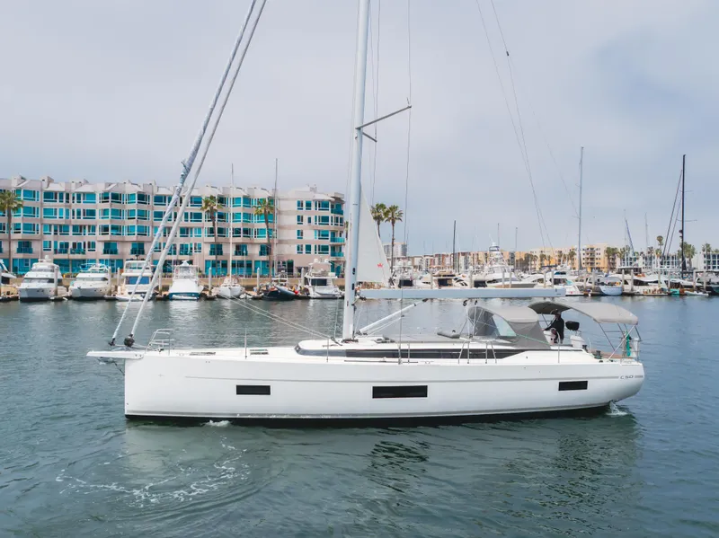 Slide: The Image of 2021 Bavaria C50 Style yacht sailing in a marina with modern buildings in the background. - 12