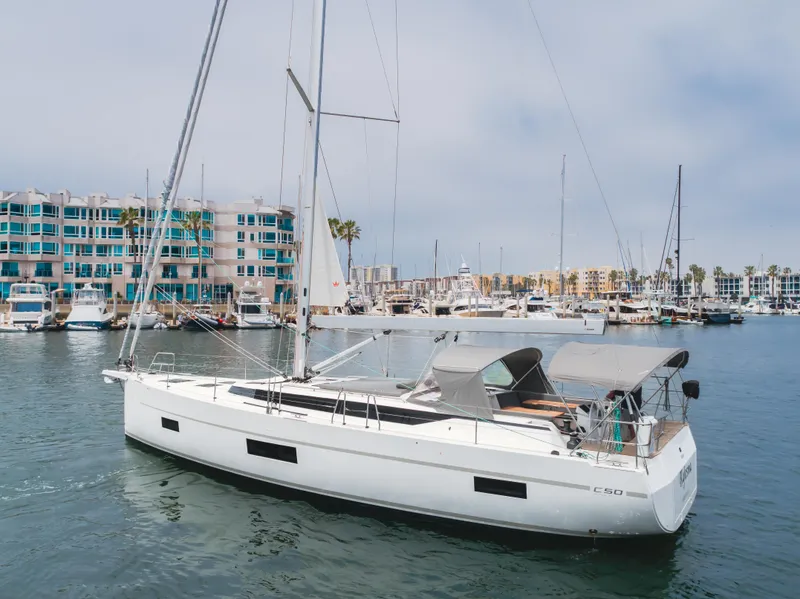 Slide: The Image of 2021 Bavaria C50 Style yacht docked in a marina with modern buildings in the background. - 13
