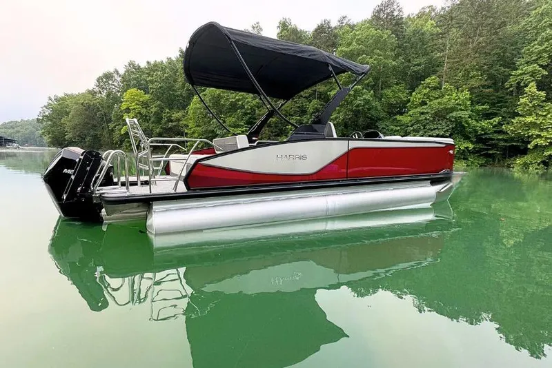 Slide: The Image of 2026 Harris Sunliner 250 SLE pontoon boat on a serene lake with lush greenery. - 2