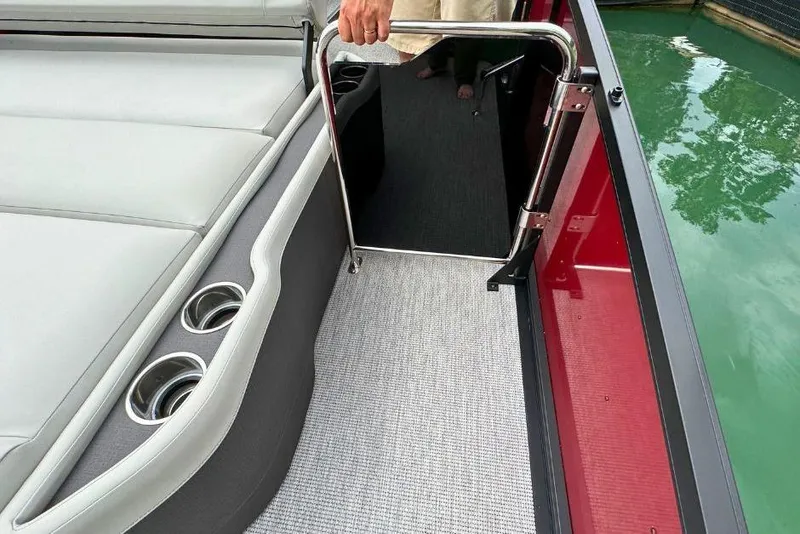 Slide: The Image of 2026 Harris Sunliner 250 SLE boat interior with seating, cup holders, and open gate by water. - 50