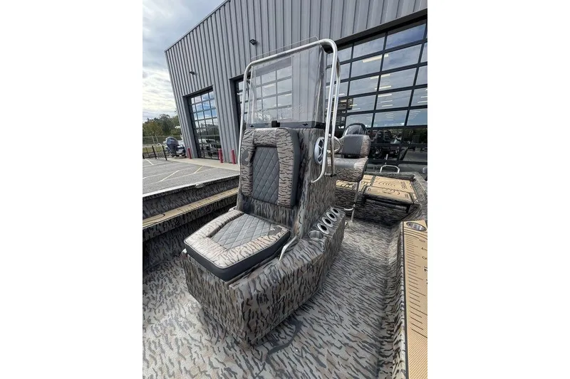 Slide: The Image of 2026 Xpress H22B Bay boat with camouflage interior, parked outside a modern building. - 13