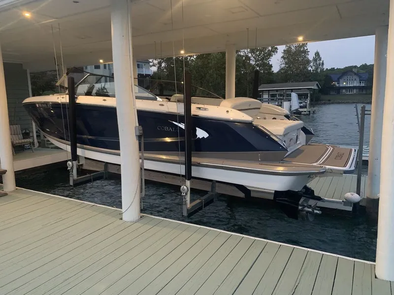 Slide: The Image of 2014 Cobalt A25 boat on lift at dock, surrounded by water and trees. - 4