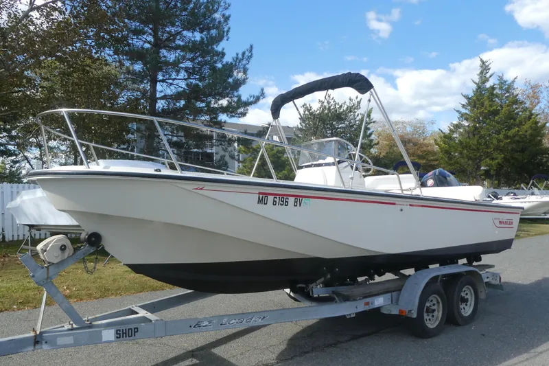 The Image of 1989 Boston Whaler 220 Outrage boat on trailer, parked outdoors under blue sky. - 1