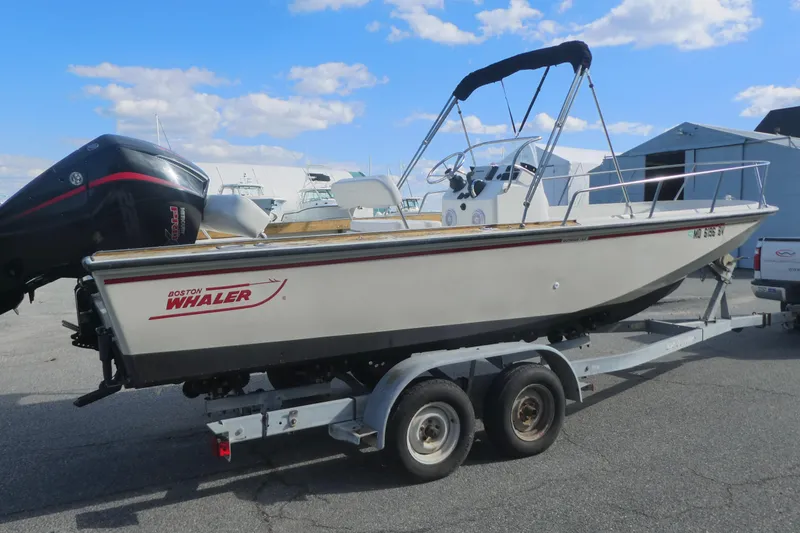 Slide: The Image of 1989 Boston Whaler 220 Outrage boat on trailer, parked outdoors under blue sky. - 3