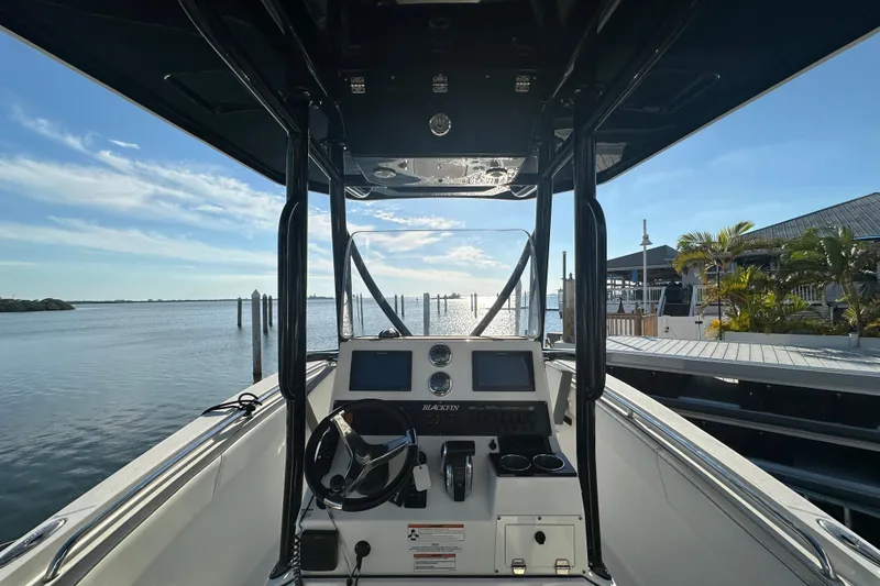 Slide: The Image of 2018 Blackfin 212 CC boat interior with steering wheel, dockside view, and clear blue sky. - 23