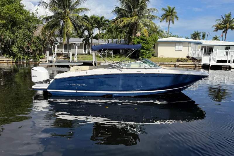 The Image of 2021 Regal 26 OBX boat on calm water with palm trees and houses in the background. - 2