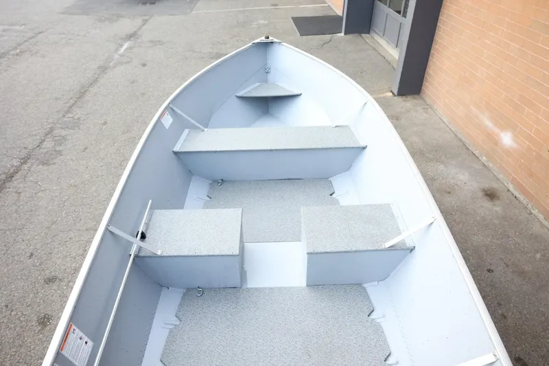 Slide: The Image of 2026 Lund SSV-16 Tiller boat interior with gray seating and flooring, parked outdoors. - 16