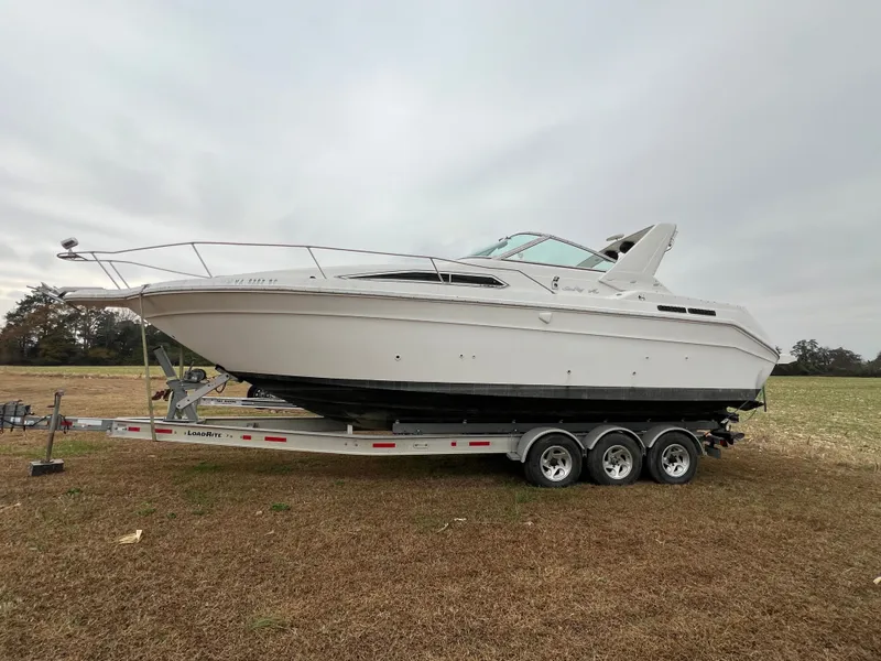 The Image of 1992 Sea Ray 300 boat on trailer in open field, overcast sky. - 0
