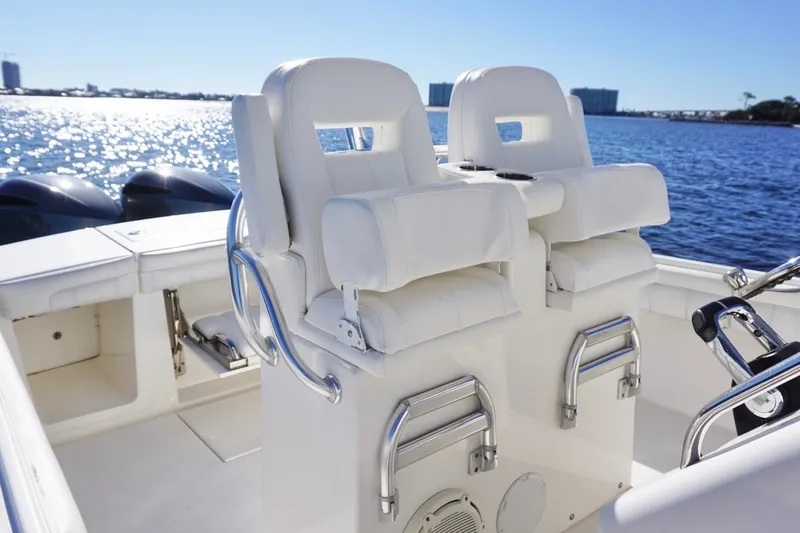 Slide: The Image of 2018 Regulator 28 boat interior with dual white captain's chairs, overlooking a sunny waterfront. - 14