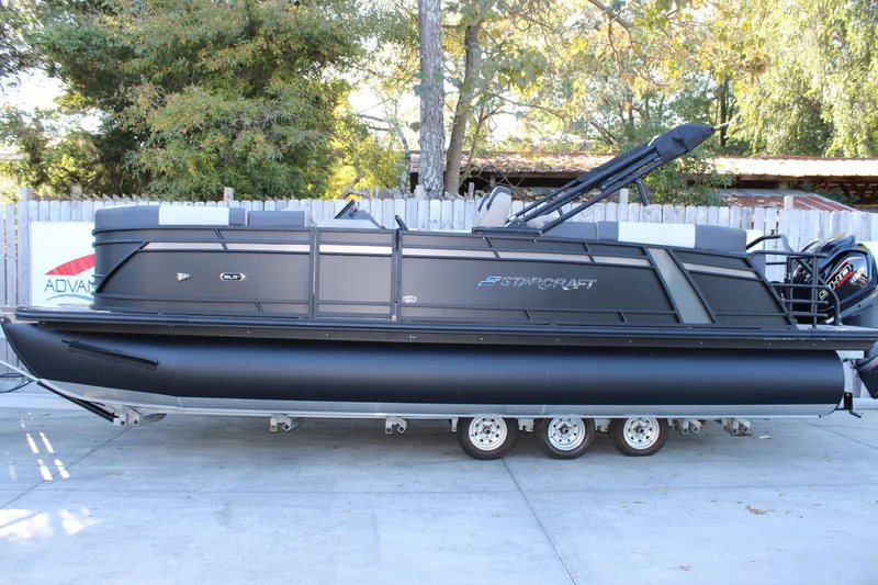 Slide: The Image of 2026 Starcraft SLS 3 pontoon boat in a driveway, surrounded by trees and a wooden fence. - 2