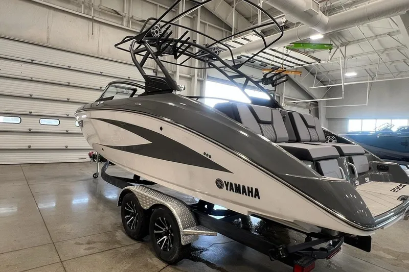 Slide: The Image of 2025 Yamaha Boats 255XE in showroom, sleek design, gray and white exterior. - 2