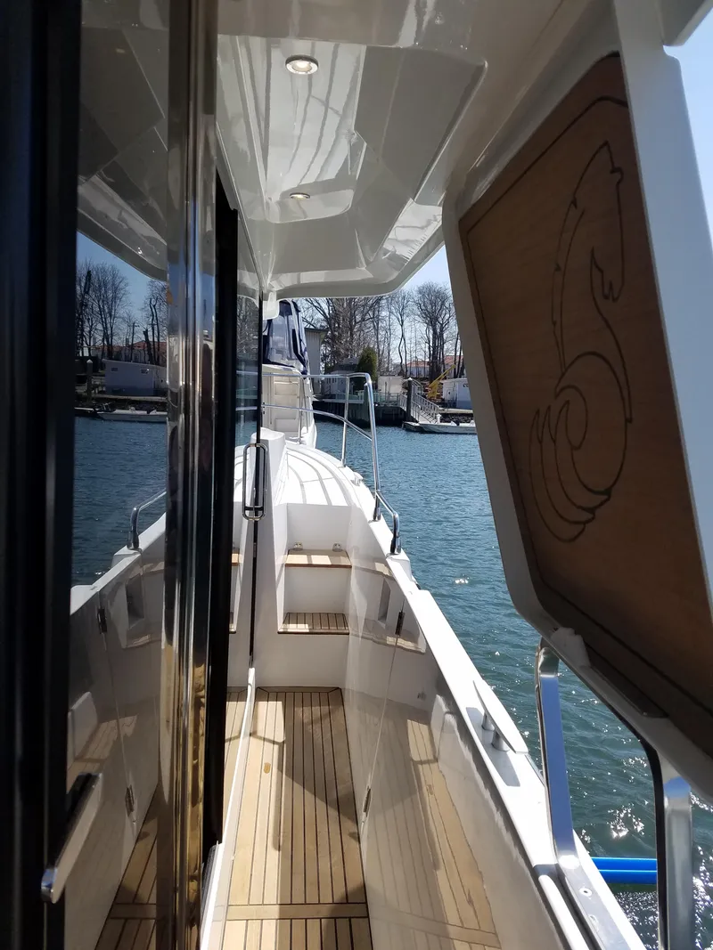 Slide: The Image of 2019 Beneteau Swift Trawler 35, side deck view with wood accents and water backdrop. - 12
