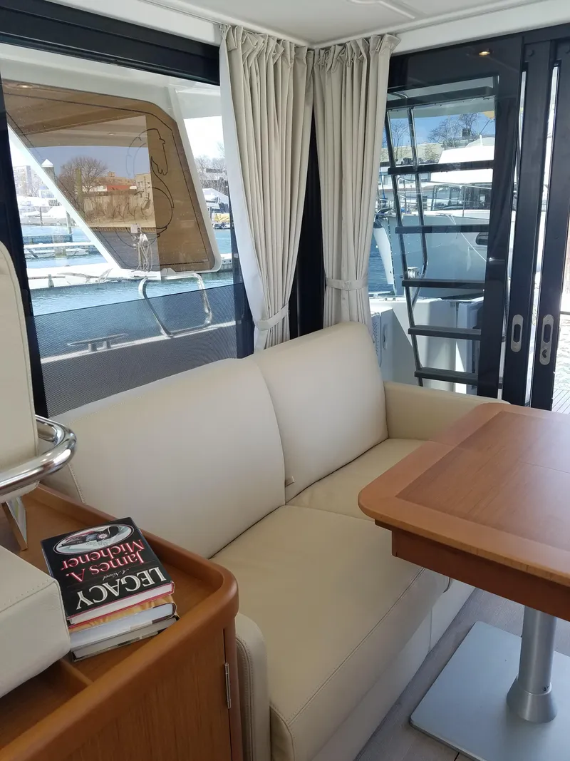 Slide: The Image of 2019 Beneteau Swift Trawler 35 interior with beige sofa, wooden table, and large windows. - 34