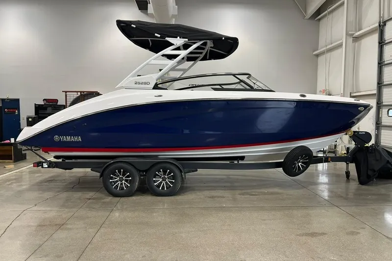 The Image of 2025 Yamaha Boats 252SD in showroom, blue and white design, on trailer. - 0