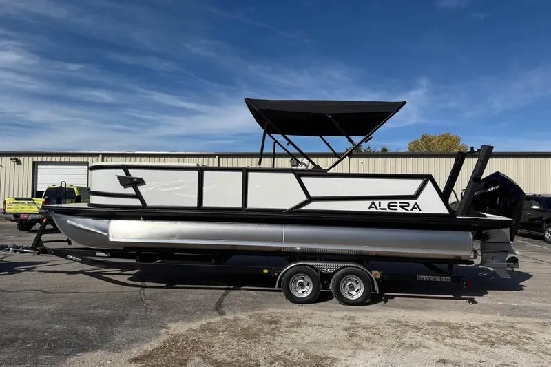 The Image of 2026 Alera M 25Q pontoon boat on trailer, parked outdoors under clear sky. - 0